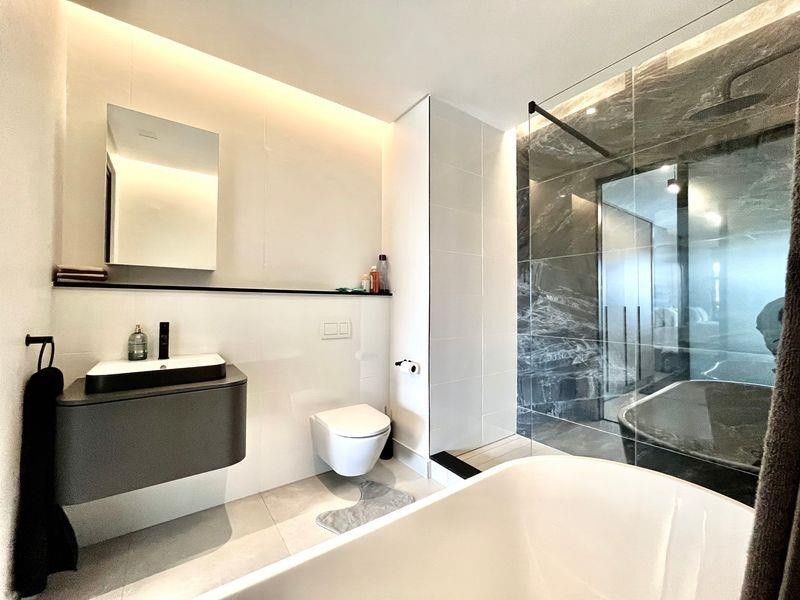 Modern bathroom featuring a wall-mounted vanity, wall-hung toilet, freestanding bathtub, and a spacious walk-in shower with dark marble-effect tiling.