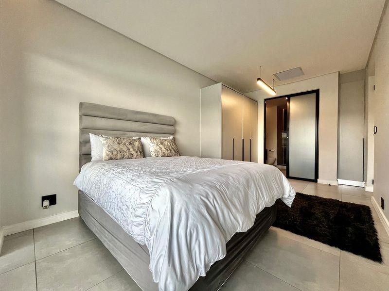 Modern bedroom featuring neutral tiled flooring, built-in cupboards, and direct access to an en-suite bathroom with a frosted glass door.