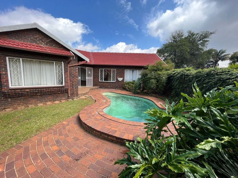 Rear exterior view of the townhouse featuring a kidney-shaped swimming pool, brick paved surround, and established garden borders.