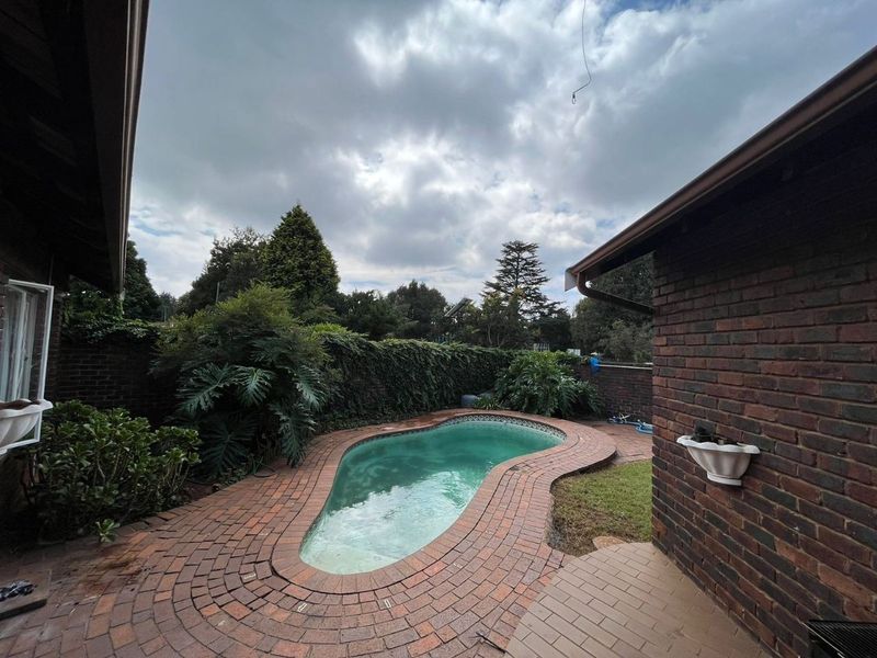 Outdoor pool area featuring a kidney-shaped swimming pool surrounded by brick paving and enclosed by a brick boundary wall.