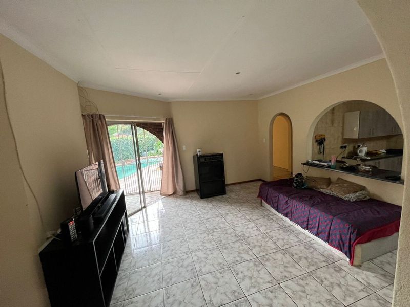 Open plan living area featuring tiled flooring, an arched pass-through to the kitchen, and sliding glass doors leading to the outdoor pool area.