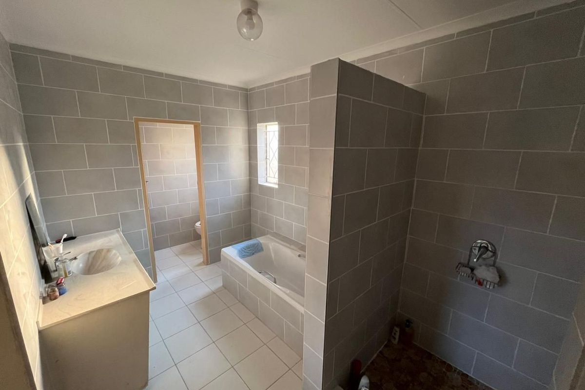 A functional bathroom featuring a built-in vanity, bathtub, and separate shower enclosure with grey wall tiling and white floor tiles.