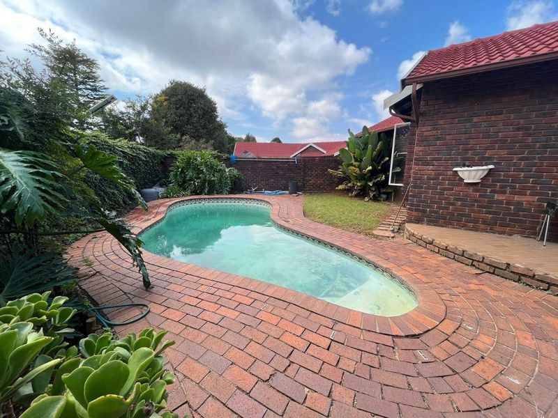 Outdoor pool area featuring a kidney-shaped swimming pool surrounded by brick paving and enclosed by a brick boundary wall.