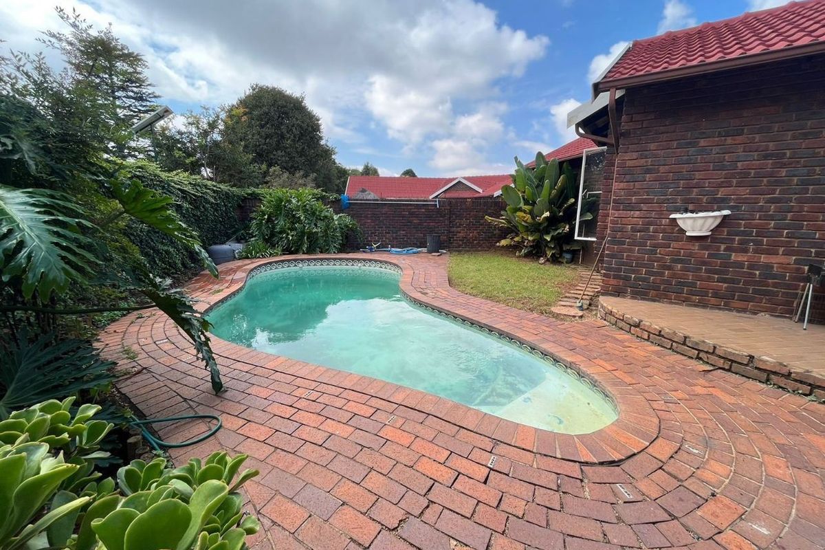 Outdoor pool area featuring a kidney-shaped swimming pool surrounded by brick paving and enclosed by a brick boundary wall.