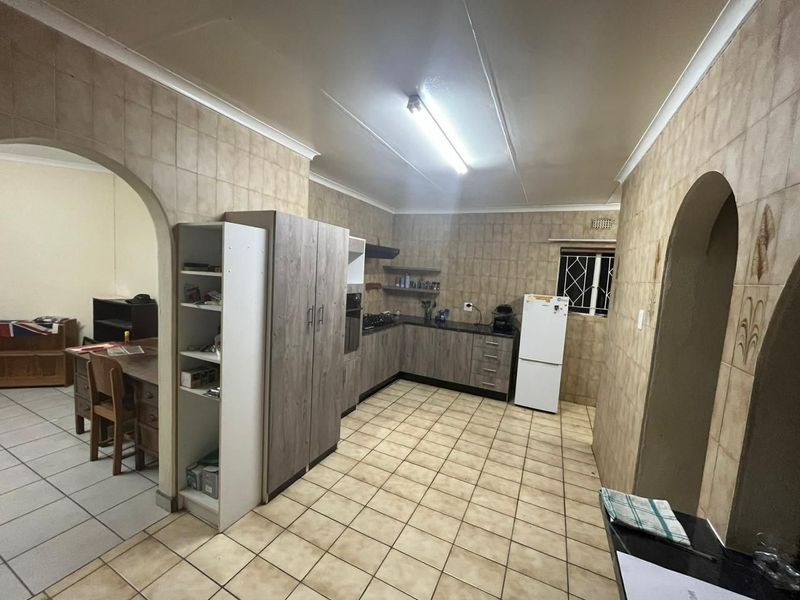 A functional kitchen featuring built-in cabinetry, laminate countertops, and tiled finishes, connected to an adjacent room via a classic archway.