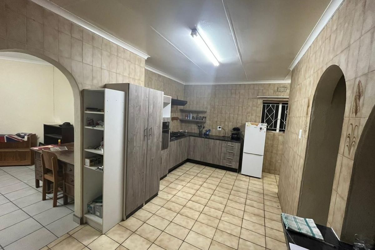 A functional kitchen featuring built-in cabinetry, laminate countertops, and tiled finishes, connected to an adjacent room via a classic archway.