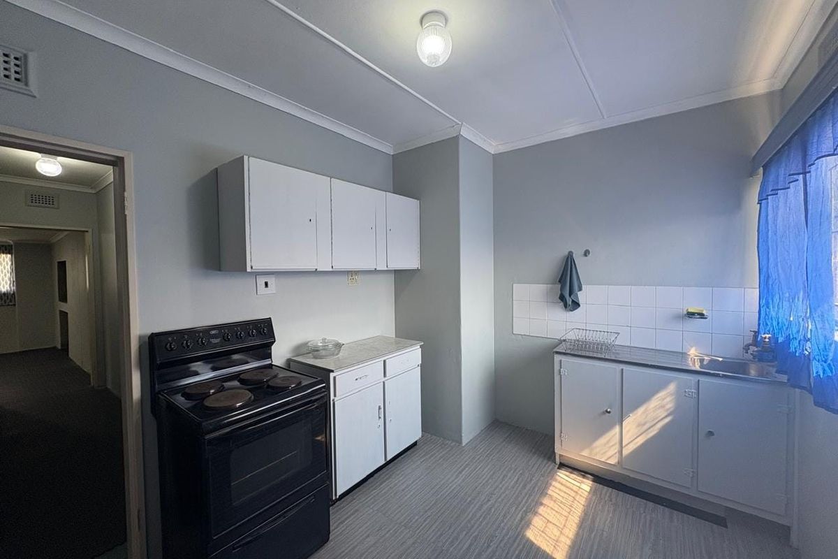 A functional kitchen featuring white cabinetry, laminate countertops, a stainless steel sink, tiled splashback, and a freestanding electric stove.