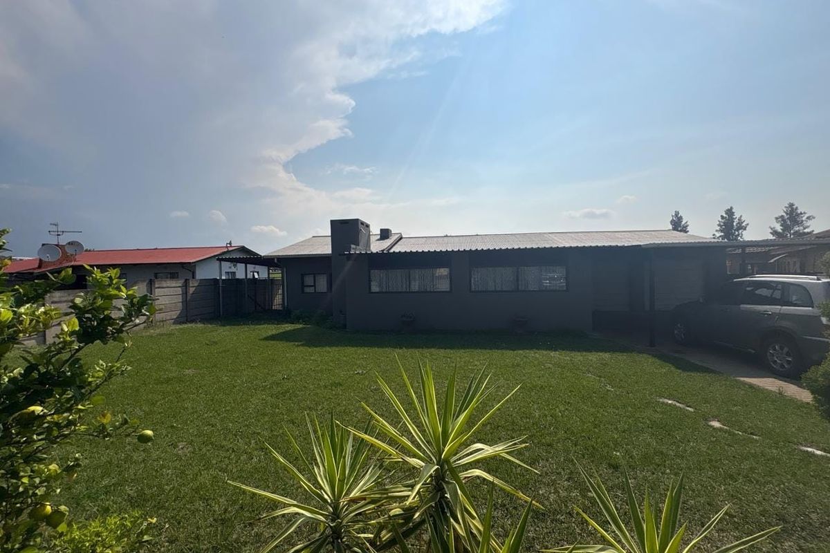 Rear view of the house featuring a corrugated metal roof, brick chimney, and a spacious lawn with a paved driveway area.