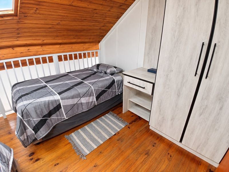 A cozy loft-style bedroom featuring warm timber ceilings, polished wooden floors, and integrated built-in cabinetry with a vanity unit.