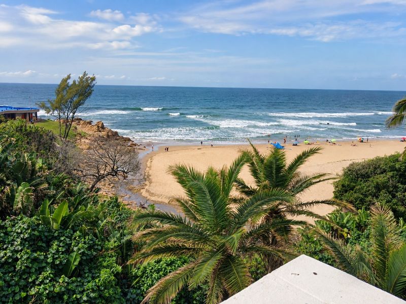 A scenic elevated view overlooking a sandy beach, ocean waves, and coastal vegetation.