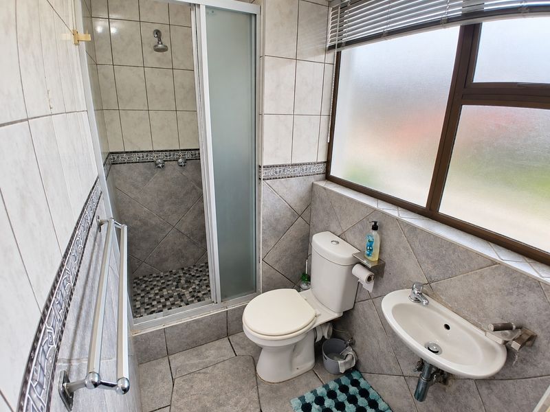 A functional bathroom featuring a shower enclosure, wall-mounted basin, and toilet, finished with neutral wall and floor tiling.