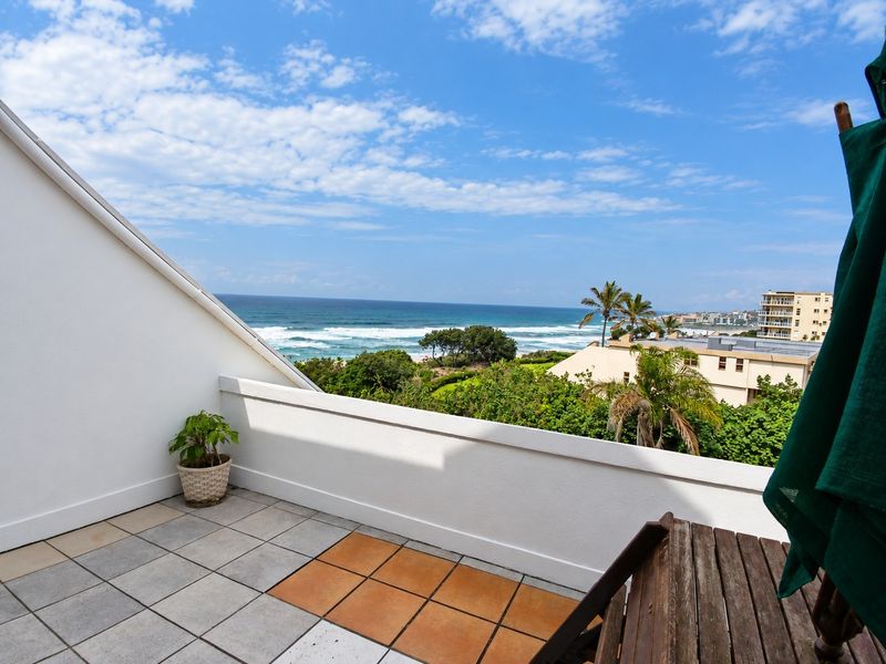 A private balcony featuring tiled flooring and a solid balustrade, offering expansive ocean and coastal views.