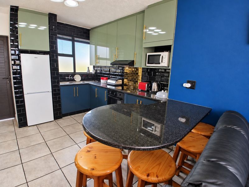 Modern kitchen featuring sage green and blue cabinetry, black subway tile backsplash, granite breakfast bar, and integrated appliances.
