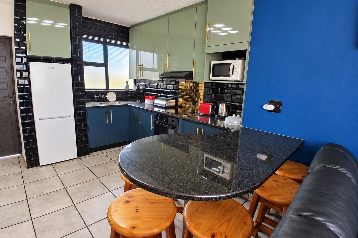 Modern kitchen featuring sage green and blue cabinetry, black subway tile backsplash, granite breakfast bar, and integrated appliances.