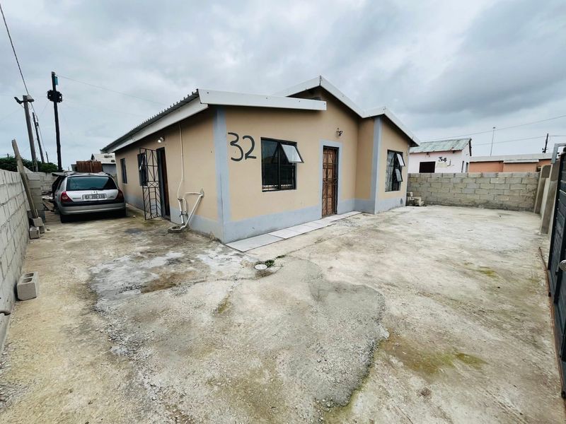 Front exterior view of a single-story house featuring a concrete driveway, perimeter wall, and security gate access.