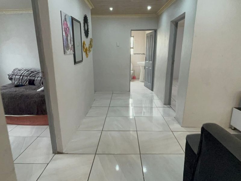 A central hallway featuring light-colored floor tiles, recessed ceiling lighting, and access to adjacent rooms including a bathroom.
