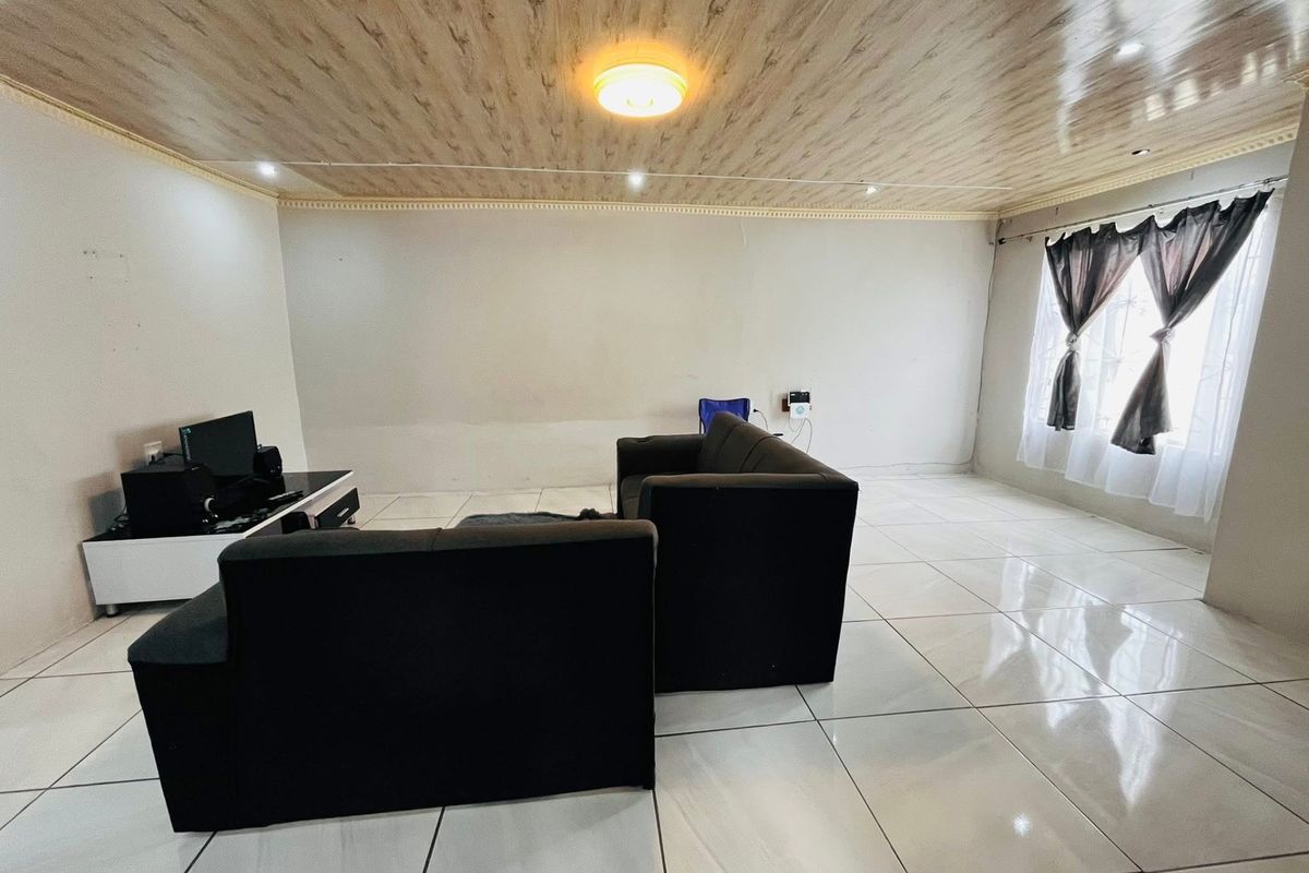 A living room featuring large white floor tiles and a wood-look paneled ceiling, providing a neutral base for interior updates.