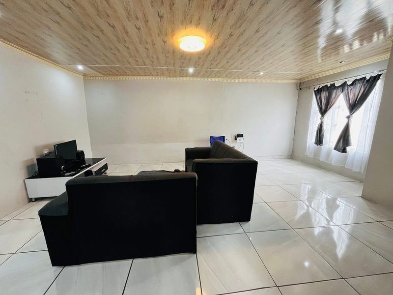 A living room featuring large white floor tiles and a wood-look paneled ceiling, providing a neutral base for interior updates.