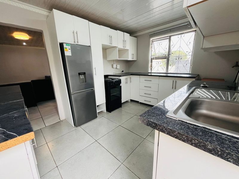 A functional kitchen featuring white cabinetry, dark laminate countertops, tiled flooring, and a stainless steel sink, with a window providing natural light.