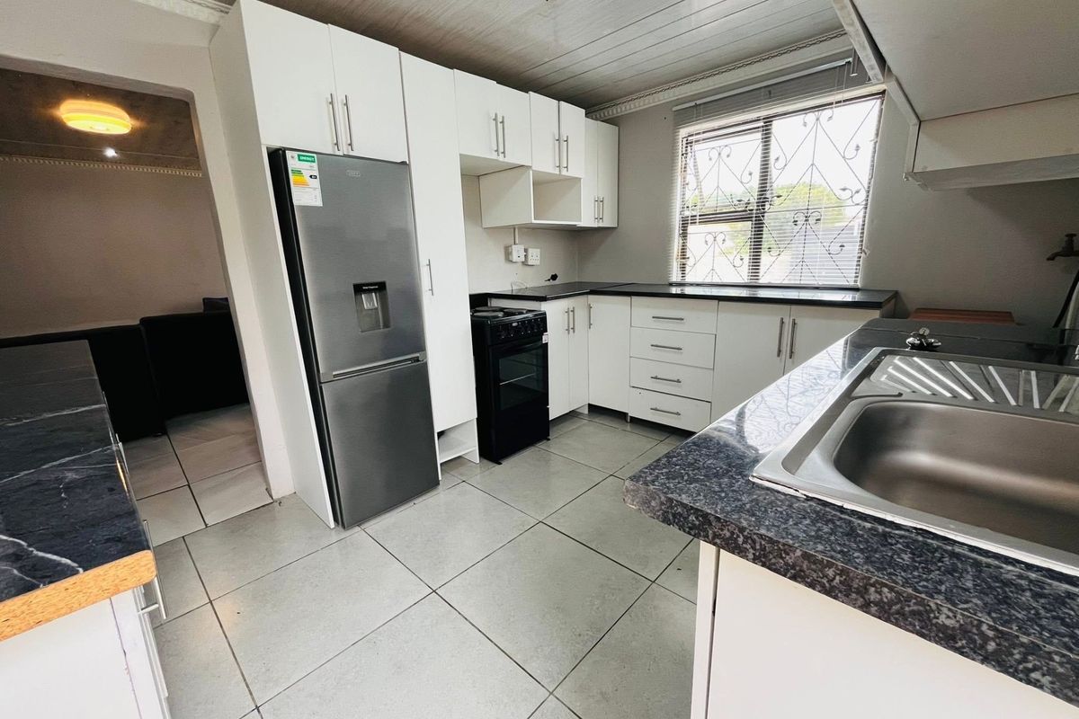 A functional kitchen featuring white cabinetry, dark laminate countertops, tiled flooring, and a stainless steel sink, with a window providing natural light.