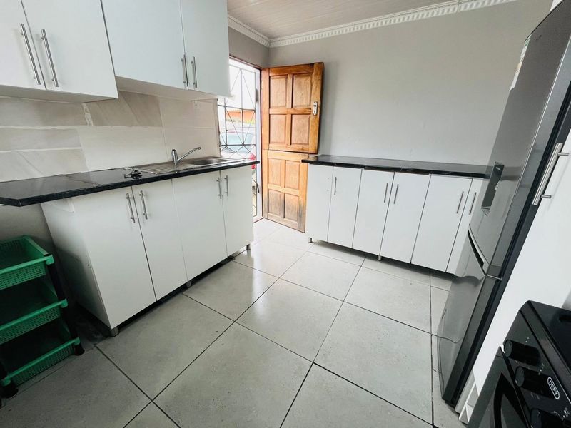 A functional kitchen featuring white built-in cabinetry, dark countertops, a stainless steel sink, and tiled flooring with direct access to the exterior.