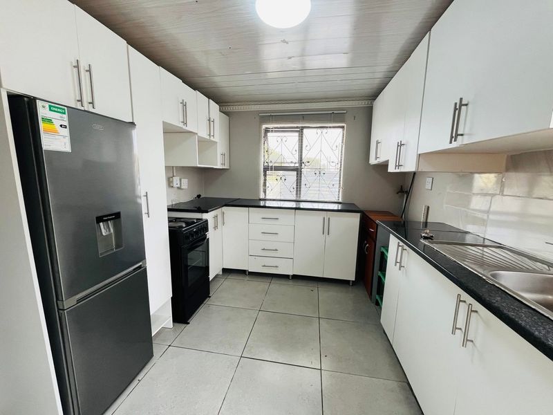 A functional kitchen featuring white cabinetry, dark countertops, tiled flooring, and a window with security bars, providing a clean and practical workspace.