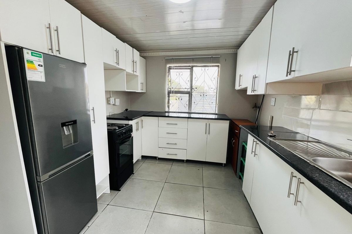 A functional kitchen featuring white cabinetry, dark countertops, tiled flooring, and a window with security bars, providing a clean and practical workspace.