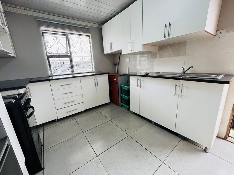 A functional kitchen featuring white cabinetry, black countertops, tiled flooring, and a window with security bars.