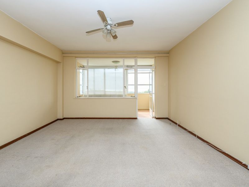 A spacious, empty living room featuring neutral walls, carpeted flooring, a ceiling fan, and direct access to an adjoining balcony area.