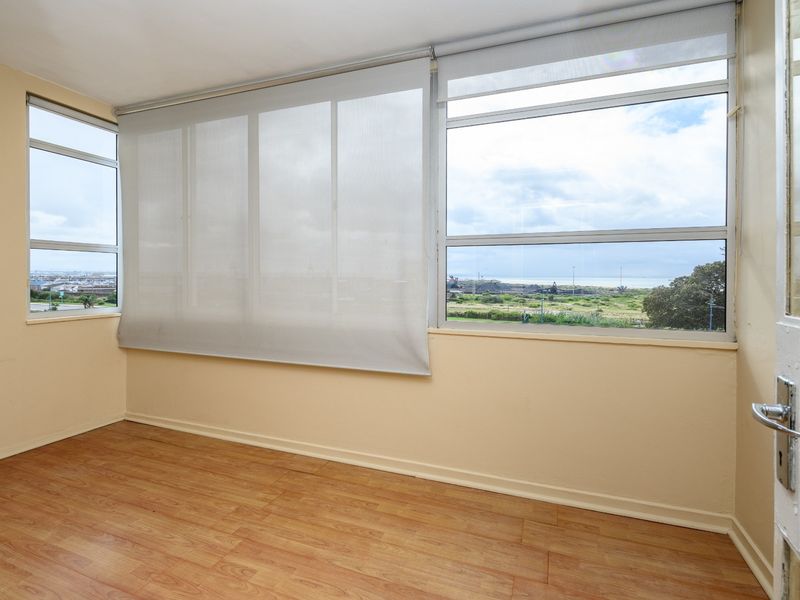 An empty living area featuring laminate flooring, large windows with roller blinds, and expansive views of the surrounding landscape.