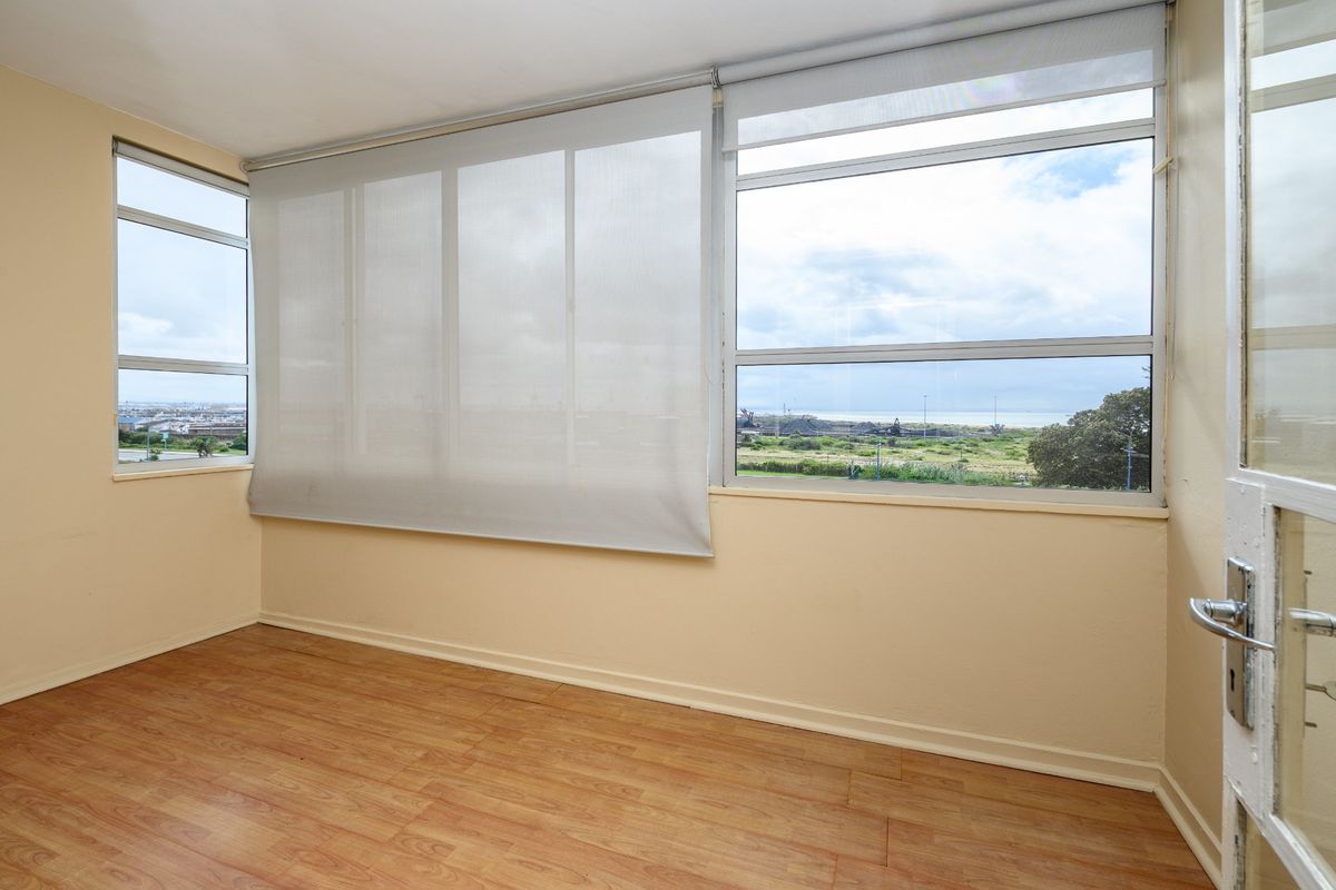 An empty living area featuring laminate flooring, large windows with roller blinds, and expansive views of the surrounding landscape.