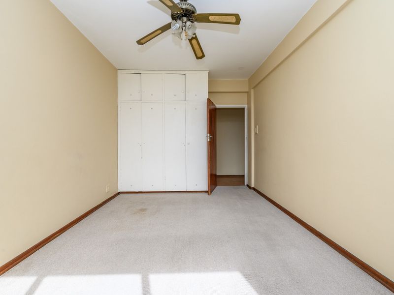 An empty bedroom featuring built-in cupboards, a ceiling fan, and carpeted flooring. The room is ready for renovation or staging.