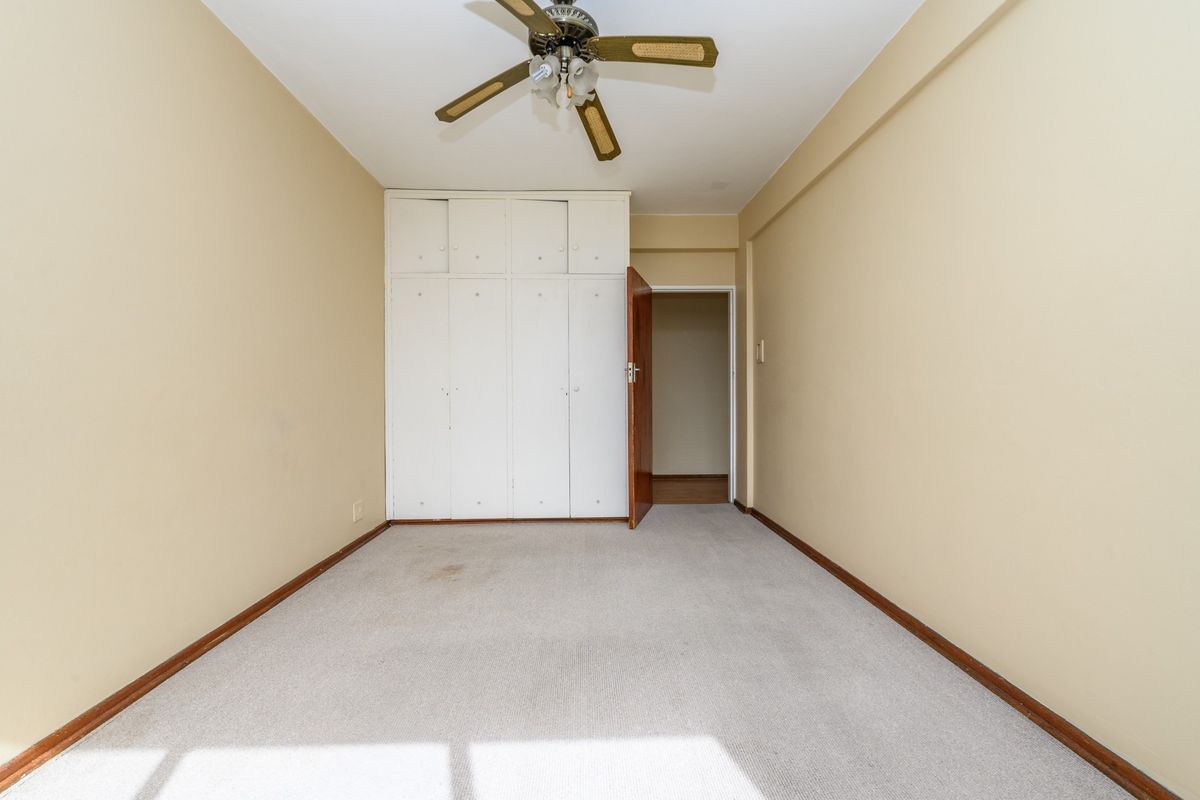 An empty bedroom featuring built-in cupboards, a ceiling fan, and carpeted flooring. The room is ready for renovation or staging.