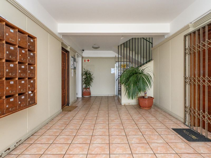 A clean apartment building entrance lobby featuring ceramic floor tiles, wall-mounted mailboxes, a security gate, and access to the elevator and staircase.