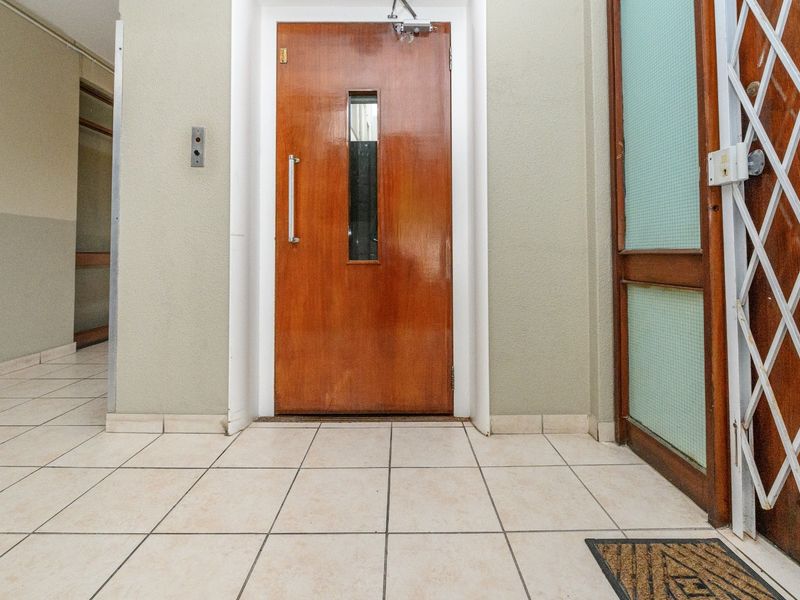 A functional apartment building hallway featuring tiled flooring, an elevator access door, and a security gate.