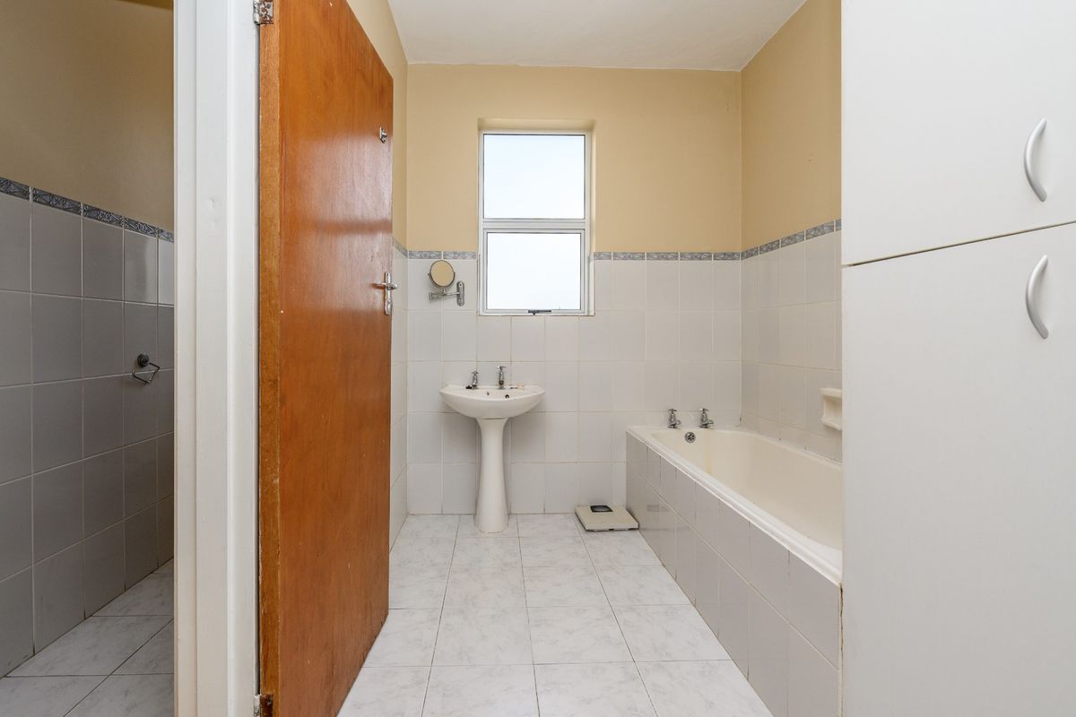 A functional bathroom featuring a pedestal basin, built-in bathtub, and tiled finishes, offering a clean and neutral space ready for modernization.