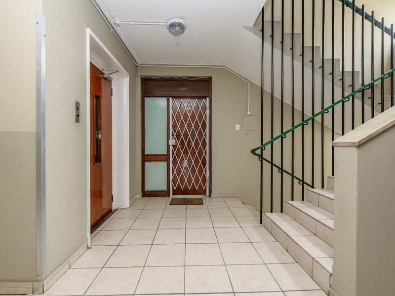 A functional apartment building entrance lobby featuring tiled flooring, a staircase with a metal handrail, and access to an elevator.