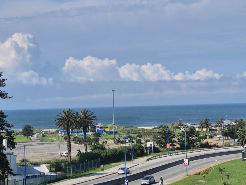 Elevated coastal view overlooking the ocean, nearby parkland, and local road infrastructure.