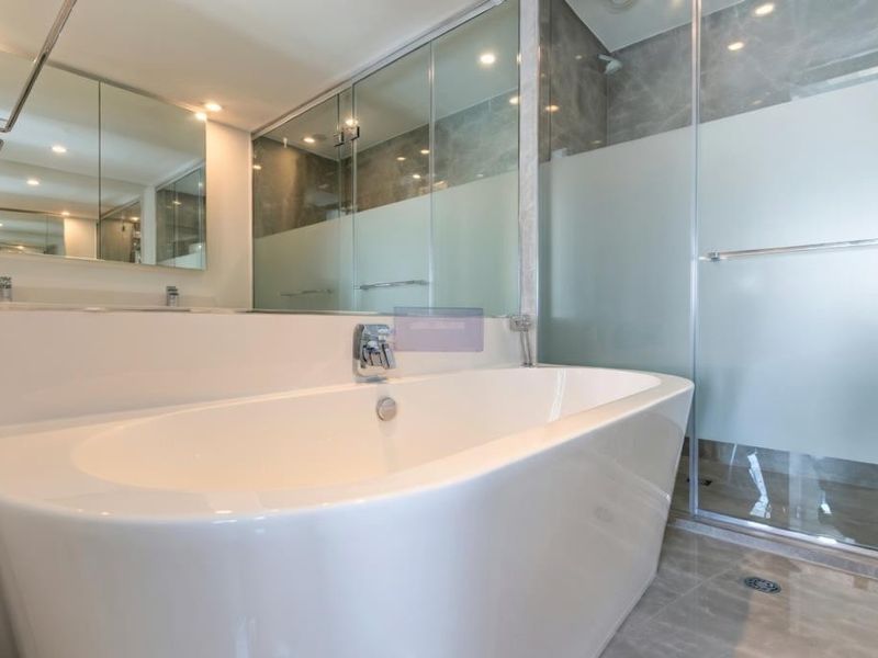 Modern bathroom featuring a sleek freestanding bathtub, a spacious glass-enclosed shower, and a large wall-mounted mirror cabinet with integrated lighting.
