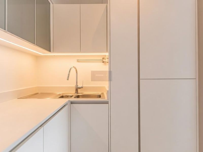 Modern, minimalist kitchen featuring sleek white cabinetry, integrated sink, and warm under-cabinet lighting, offering a clean and functional workspace.