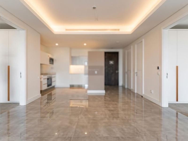 A bright, modern open-plan living and kitchen area featuring high-gloss tiled flooring, recessed cove lighting, and sleek built-in cabinetry with integrated appliances.
