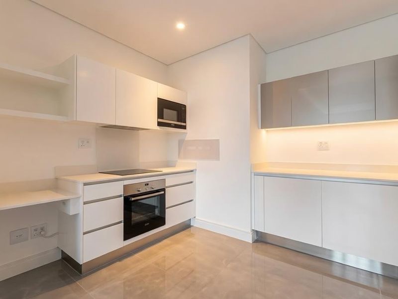 Modern, minimalist kitchen featuring sleek white cabinetry, integrated appliances including an oven and microwave, and polished tiled flooring with under-cabinet lighting.