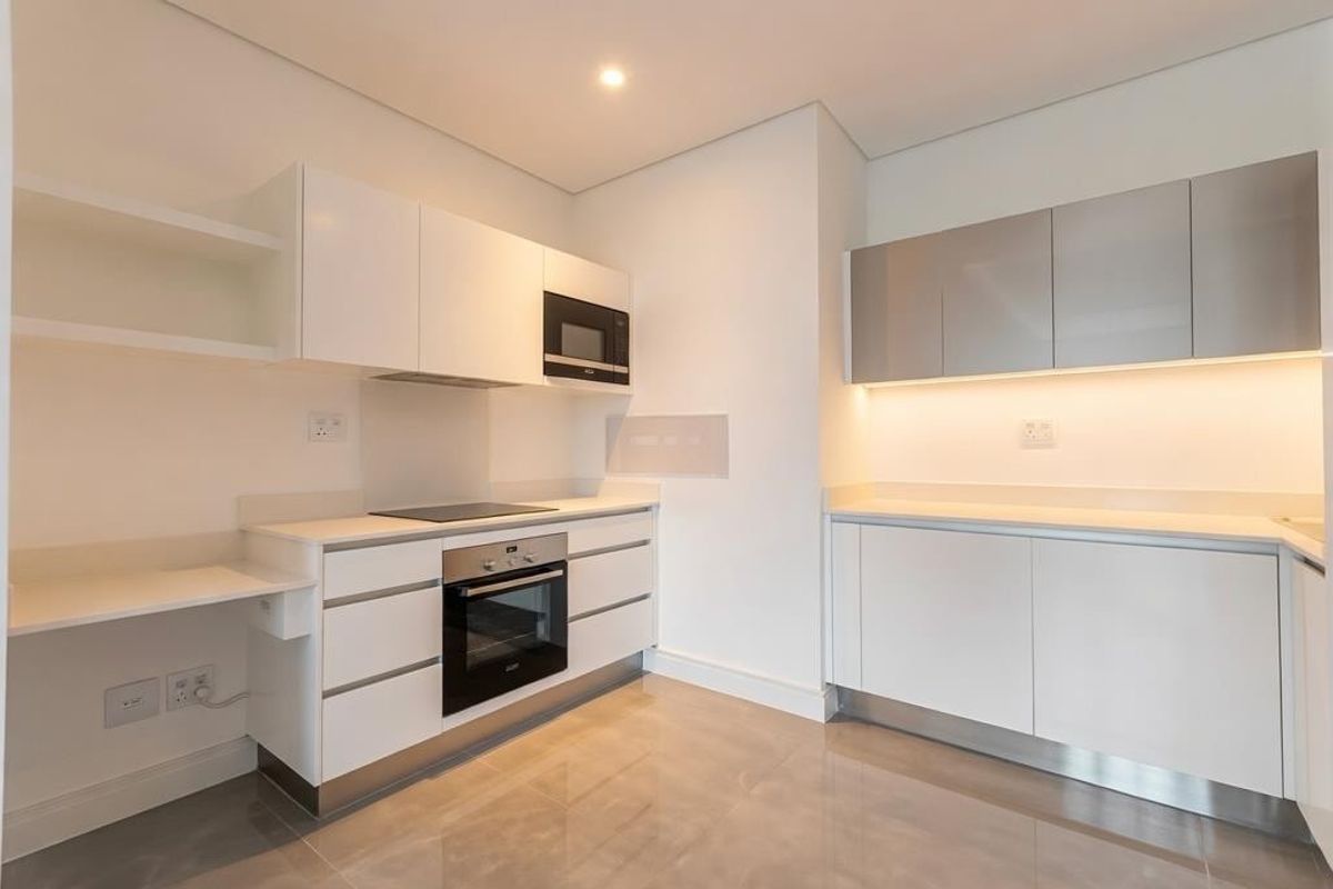 Modern, minimalist kitchen featuring sleek white cabinetry, integrated appliances including an oven and microwave, and polished tiled flooring with under-cabinet lighting.
