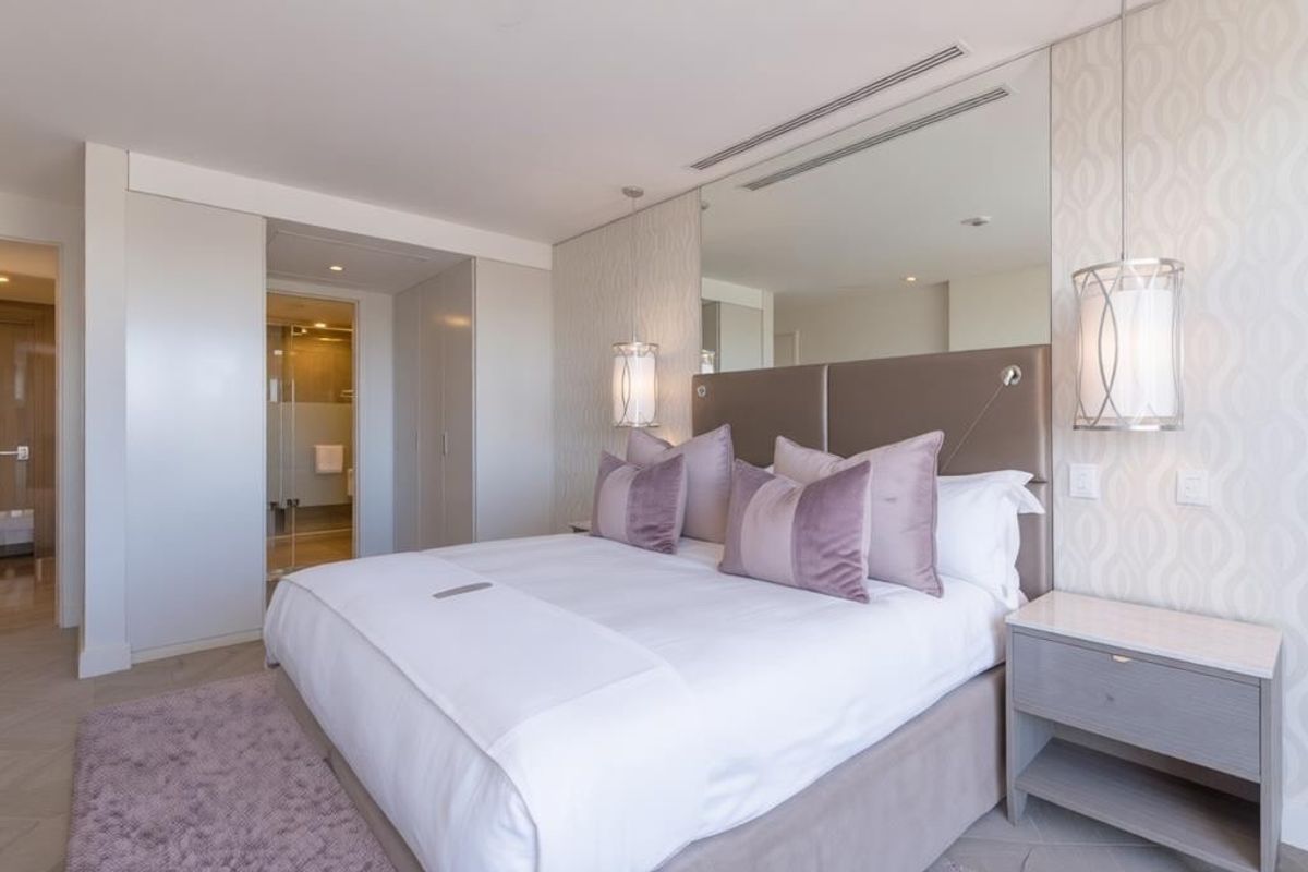 A modern, well-appointed bedroom featuring built-in wardrobes, recessed lighting, a mirrored feature wall, and direct access to an en-suite bathroom.