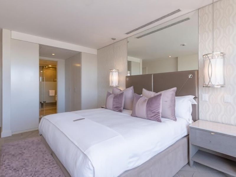 A modern, well-appointed bedroom featuring built-in wardrobes, recessed lighting, a mirrored feature wall, and direct access to an en-suite bathroom.