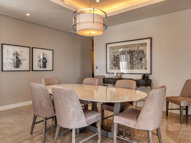 A well-appointed dining room featuring elegant tiled flooring, a recessed ceiling with cove lighting, and a modern pendant light fixture.
