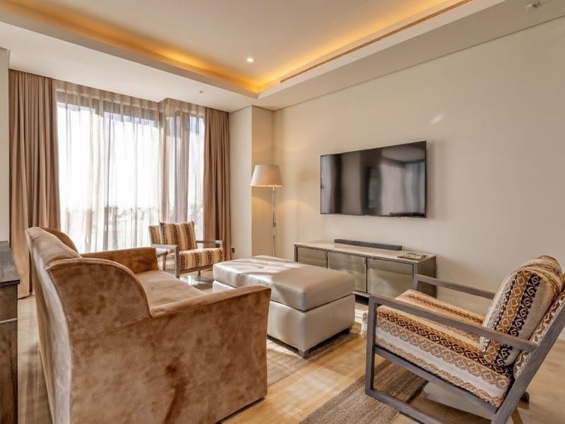 A modern, well-lit living room featuring stone flooring, recessed cove lighting, and large windows that provide ample natural light.