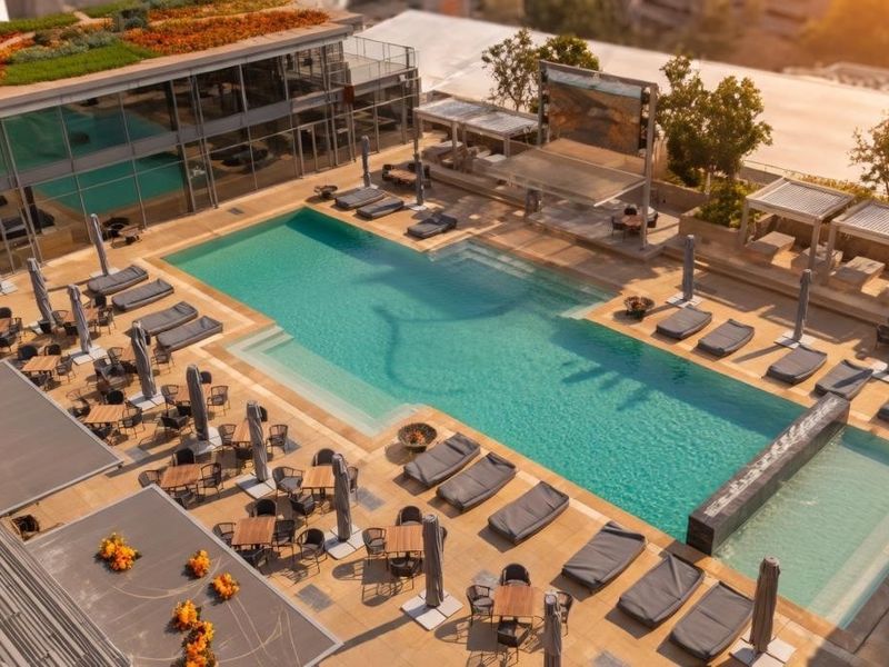 An elevated aerial view of a modern apartment complex pool area featuring a large swimming pool, tiled deck, and landscaped green roof.