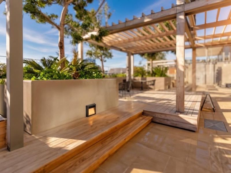 A modern, well-maintained outdoor patio featuring timber decking, a pergola structure, and integrated planter boxes with recessed lighting.