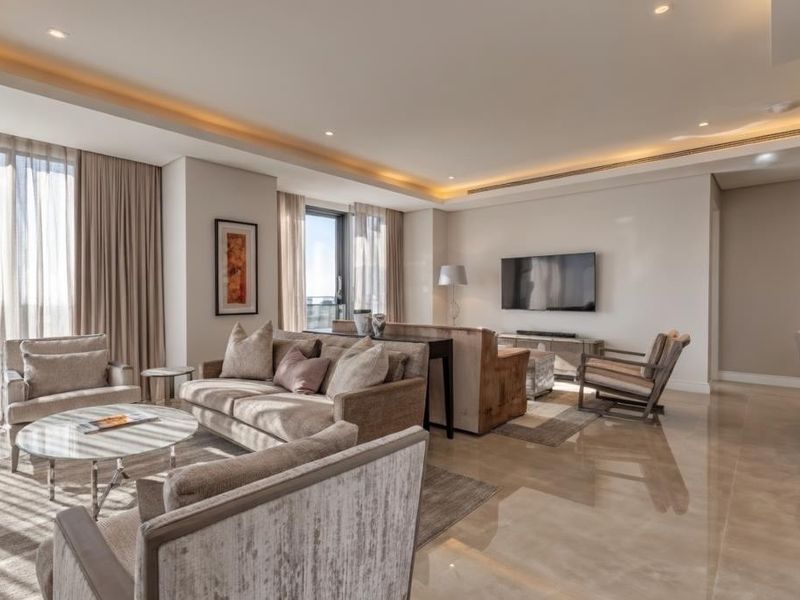A spacious, modern living room featuring high-quality large format floor tiles, recessed cove lighting, and floor-to-ceiling window treatments.